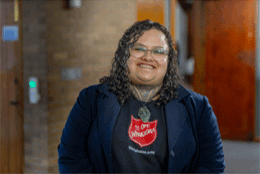 A Māori woman with chin and neck moko smiles in a Salvation Army t-shirt
